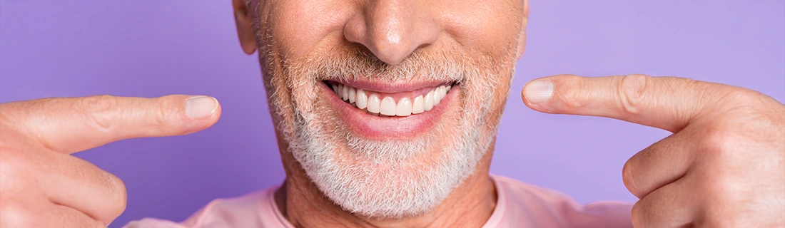 Close-Up Of A Man Pointing To His Teeth On Soft Purple Background